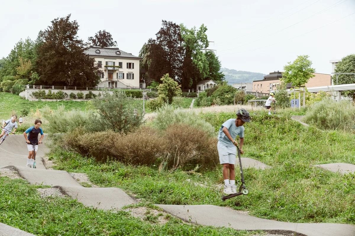 Kinder mit Scootern fahren auf einem Pumptrack.